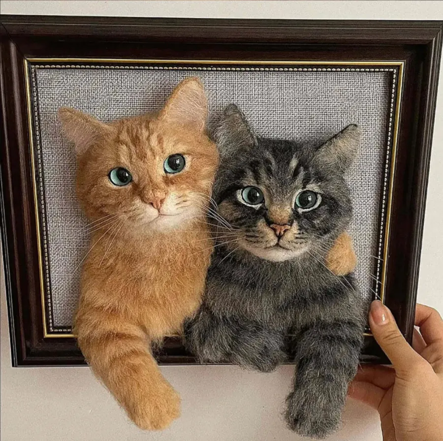 A framed portrait of two cats held in a hand.